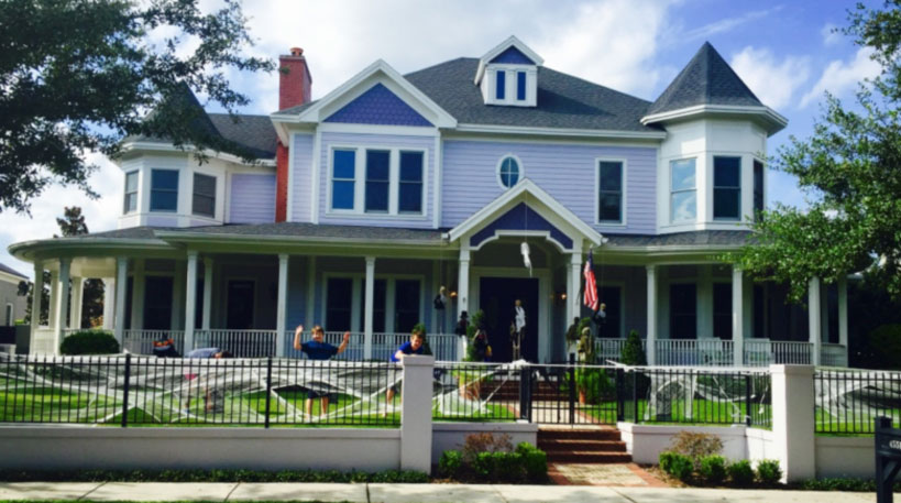 A lavender Victorian house decorated with giant spider webs for Halloween