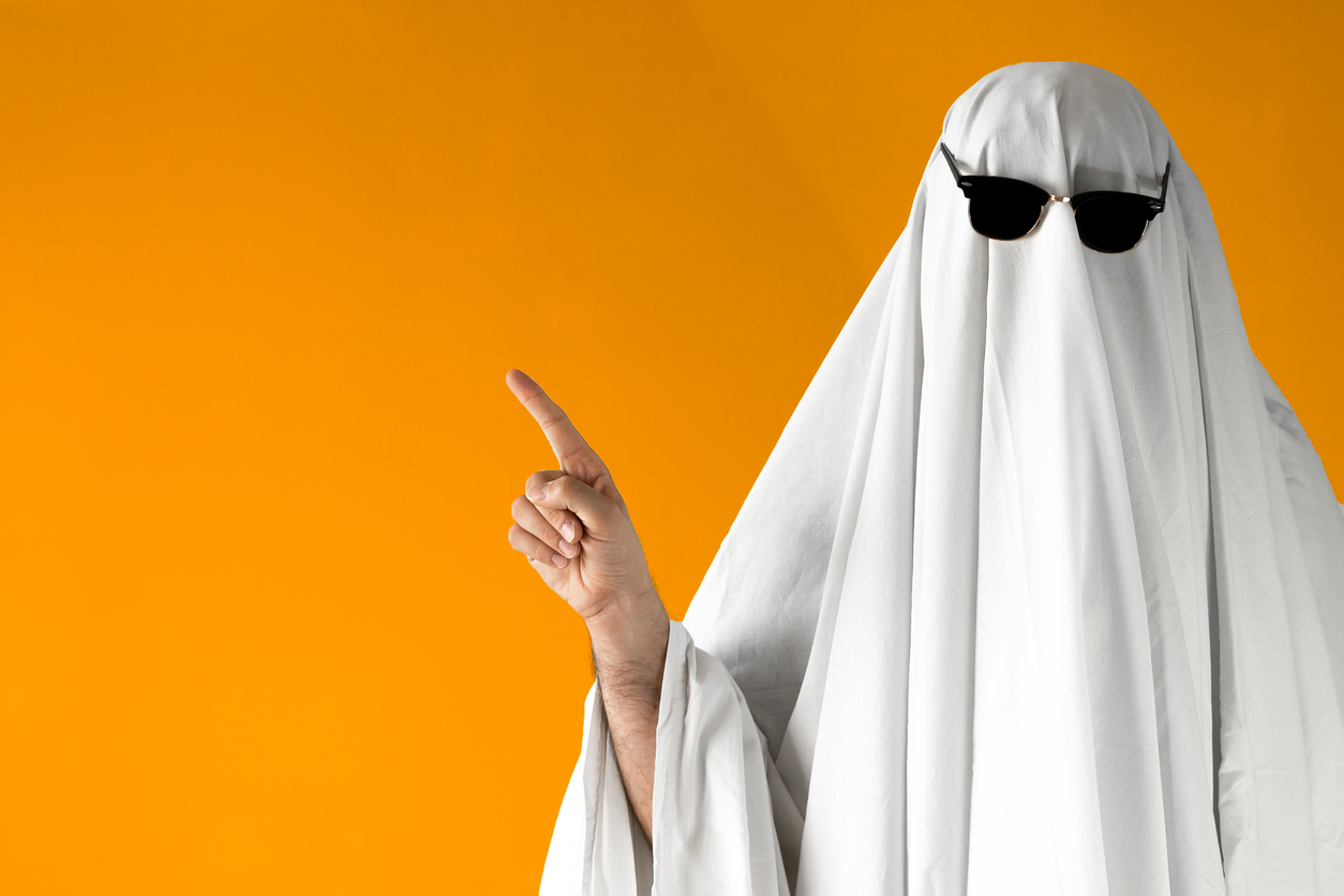 Person in Halloween costume of ghost with sunglasses points away - How